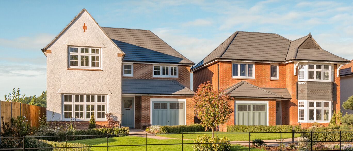 Two modern detached houses with brick and white cladding, surrounded by a well-maintained garden and a low fence, under a clear blue sky.