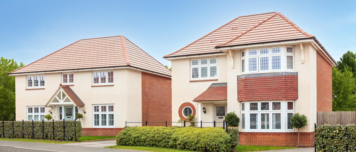 Two modern detached houses with cream and red brick exteriors, pitched roofs, bay windows, and small front gardens under a clear blue sky.