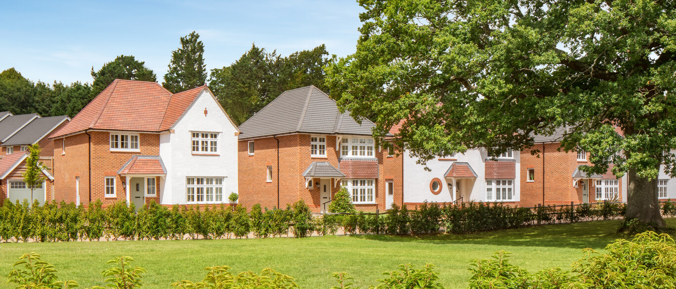 Modern residential houses with red and white brick exteriors, surrounded by greenery under a clear blue sky.