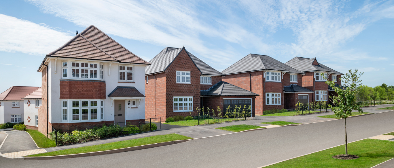 Modern suburban houses with red and grey brick exteriors, well-maintained lawns and driveways on a bright, clear day at Maes yr Haf at Plasdwr