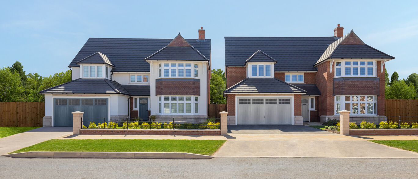 Two modern detached houses with brick and white facades, large bay windows, and well-maintained front gardens under a clear blue sky at Blossoms, Round Hill Gardens.