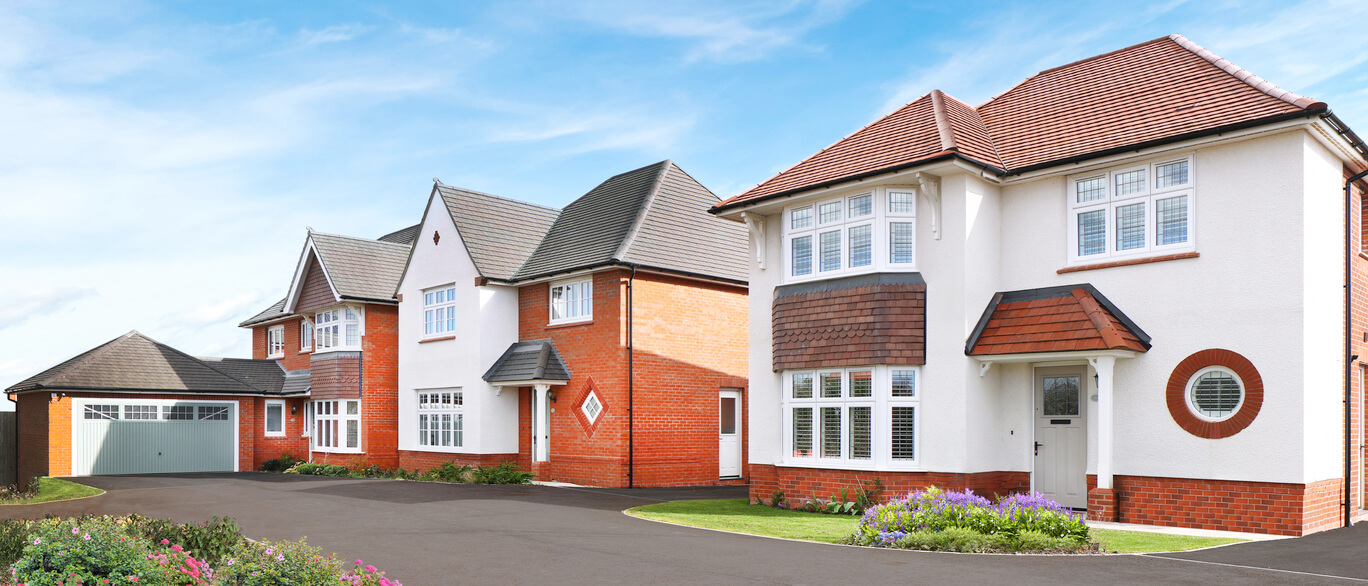 Modern residential houses with white walls, red brick accents, and pitched roofs, set against a blue sky in Kings Moat Garden Village at Roman Green at Kings Moat Garden Village.