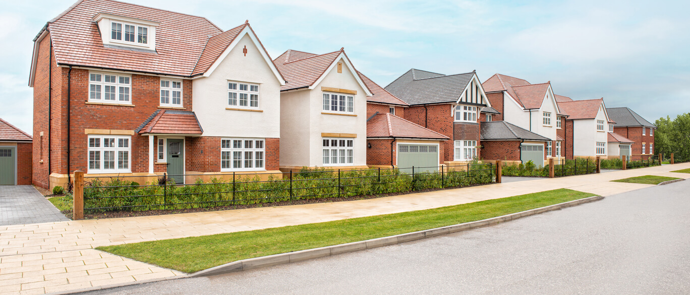 Row of modern detached houses with brick and white facades, red tiled roofs, and small front gardens on a quiet suburban street at Tabley Park.