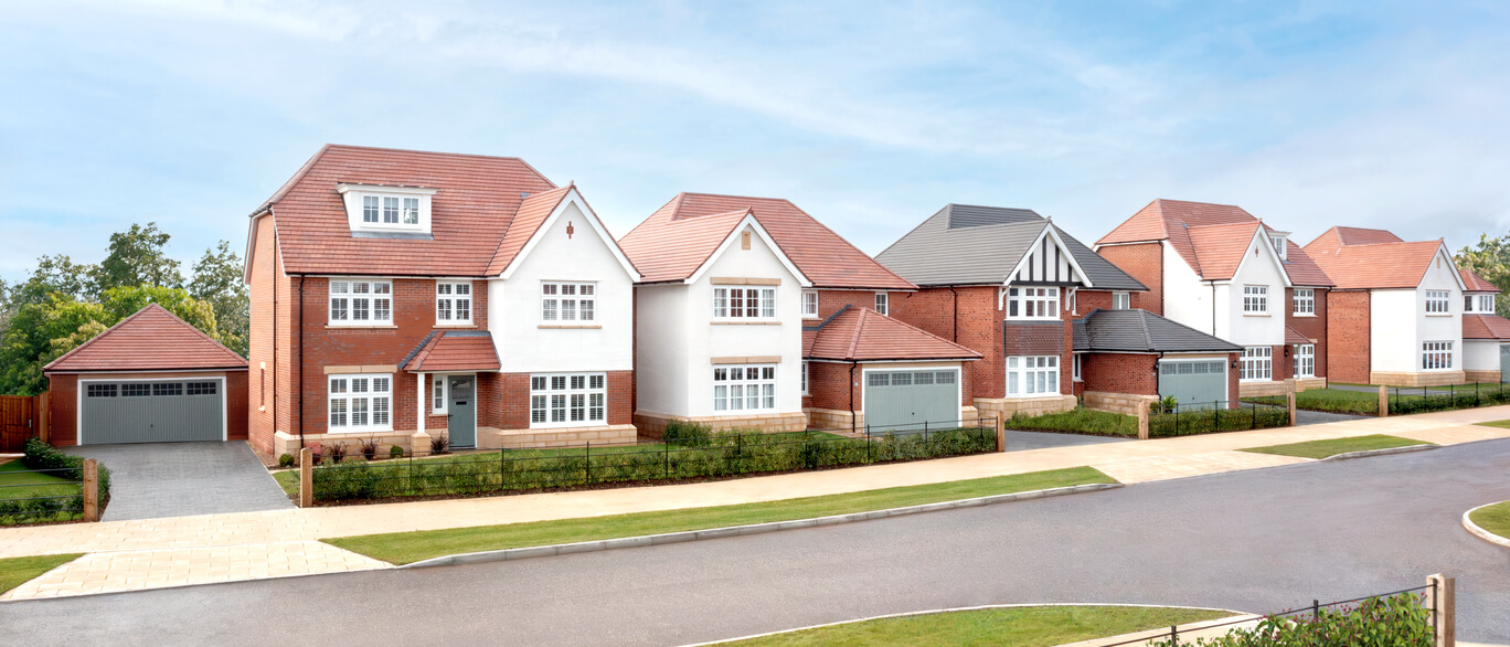 A row of modern detached houses with white and brick facades, set in a well-maintained neighbourhood with a paved road and greenery at Tabley Park.