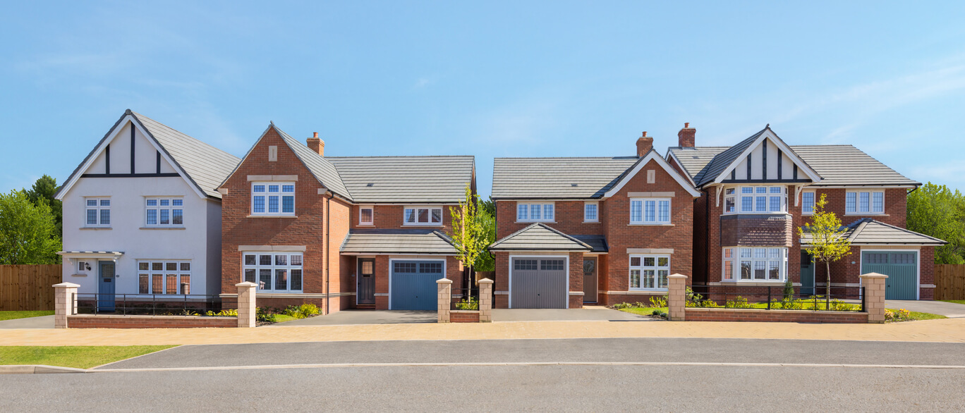 A row of modern detached houses with red brick exteriors, white and black timber detailing, and well-maintained front gardens and driveways at Woodlands, Round Hill Gardens.