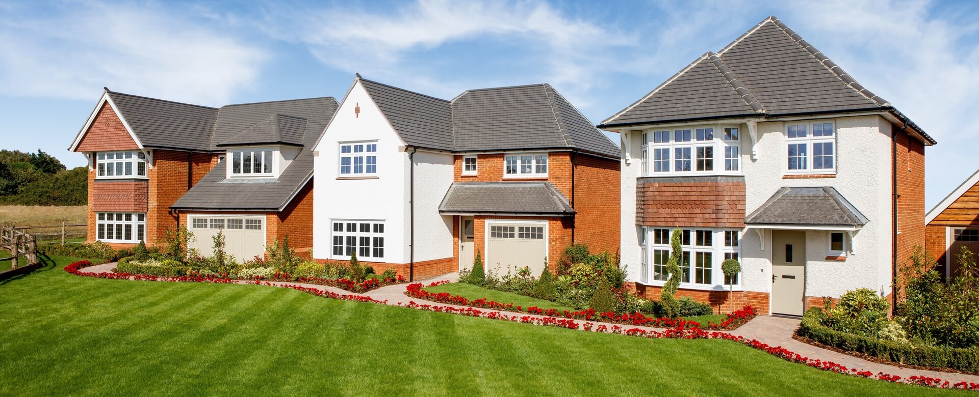 A row of modern detached houses with driveways and well-maintained front gardens under a blue sky at Amber Fields.