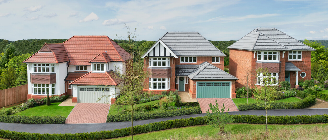 Three large detached houses with colourful brick and tile exteriors, surrounded by landscaped gardens and a winding driveway, set against green rolling hills at Preston Fields.