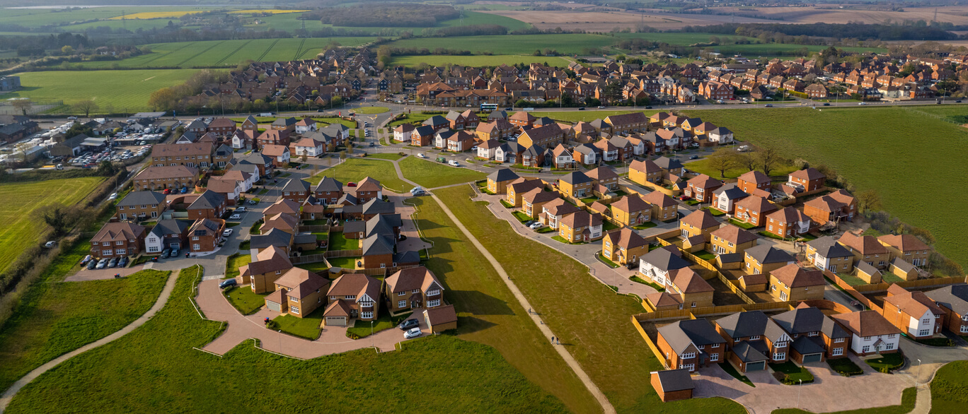 Modern residential houses with brick and timber cladding, surrounded by green lawns and trees under a blue sky, with children and adults enjoying the area at The Hoplands.