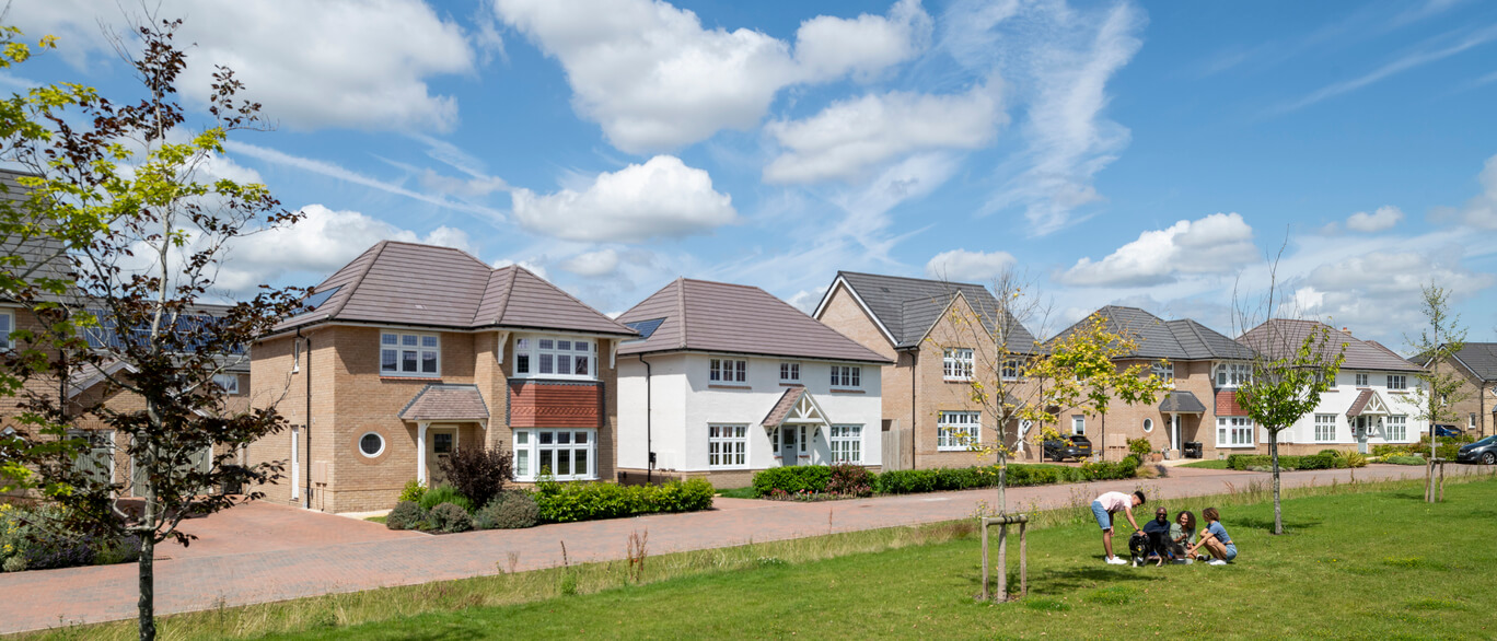 Suburban street with modern detached houses, green lawn, and children playing in a park under a blue sky with fluffy clouds at All Saints Gardens.
