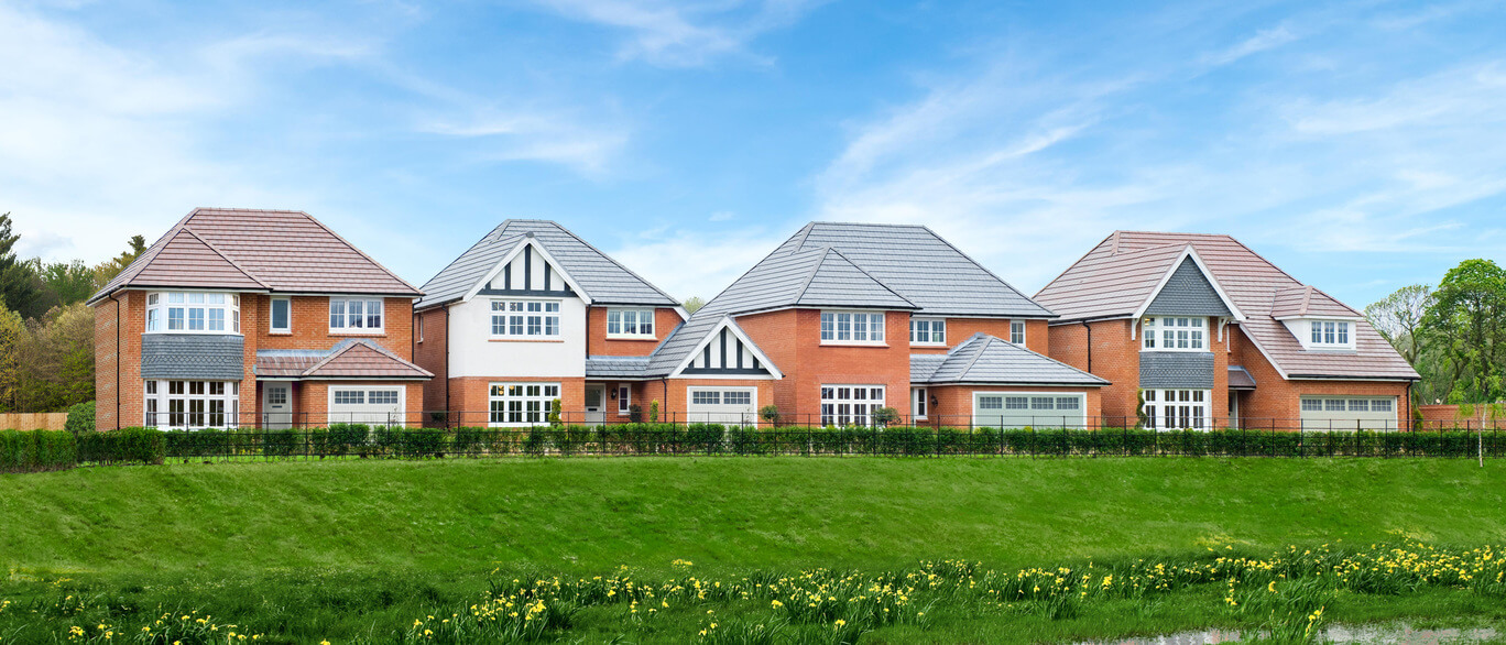 Modern detached houses with red and grey roofing, set behind a green lawn with yellow flowers and a clear blue sky in the background.