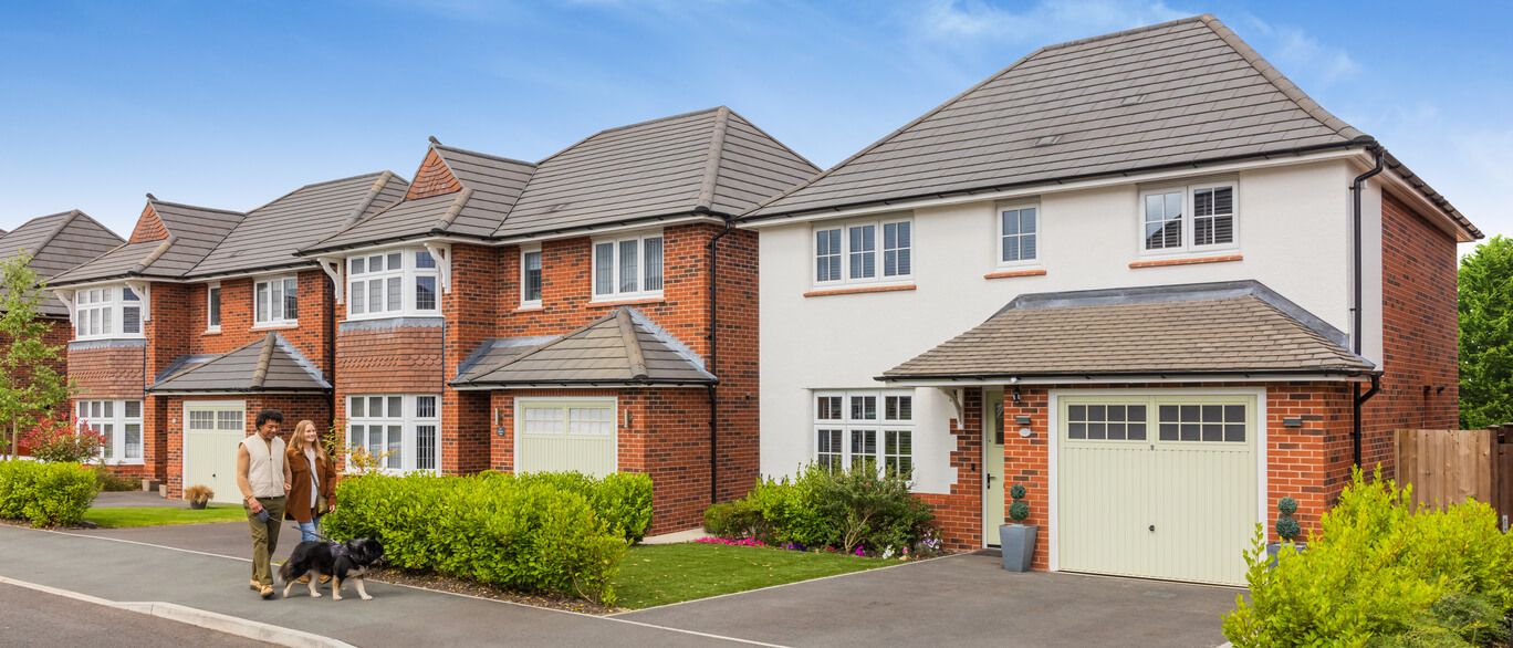 Modern red brick and white rendered semi-detached houses with grey tiled roofs at Thorpe Park, with a couple walking dogs in the front garden.