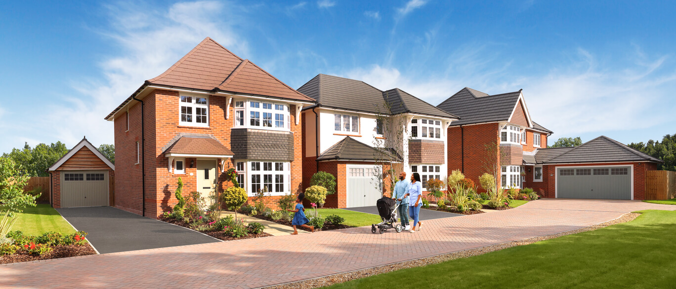Modern red-brick houses with grey rooftops, surrounded by well-kept gardens and a family walking on a paved driveway under a blue sky.