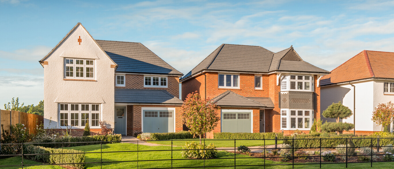 Modern detached houses with well-maintained gardens and driveways, located in a suburban neighbourhood under a blue sky.