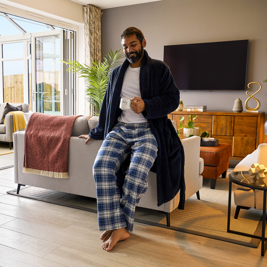 Man leaning on sofa with cuppa bare footed in his new home that has underfloor heating