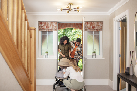 Mother and Father pushing pram through front door being greeted by a friend