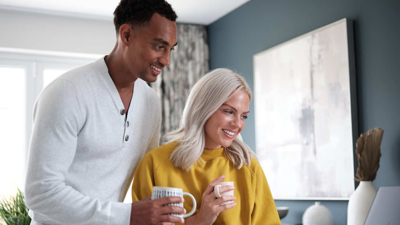 Couple smiling and drinking hot rinks while looking at a laptop