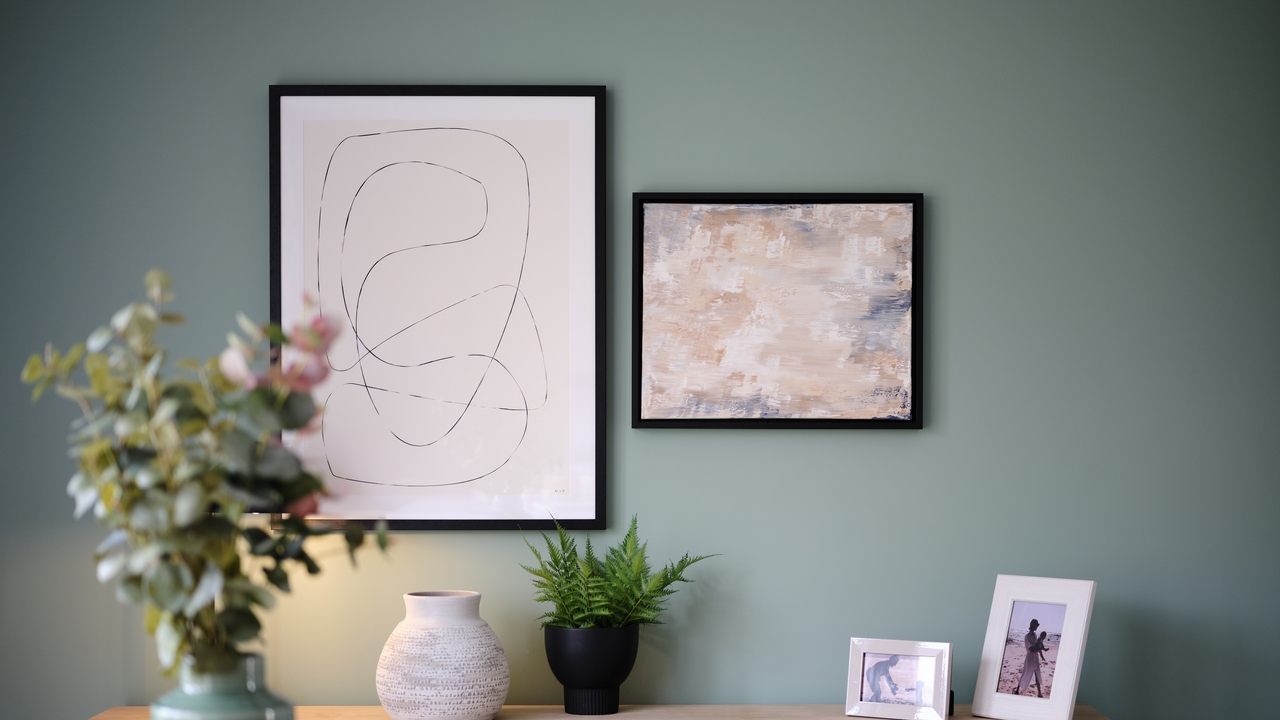 Wall art hung over a sideboard with plants and photos on it