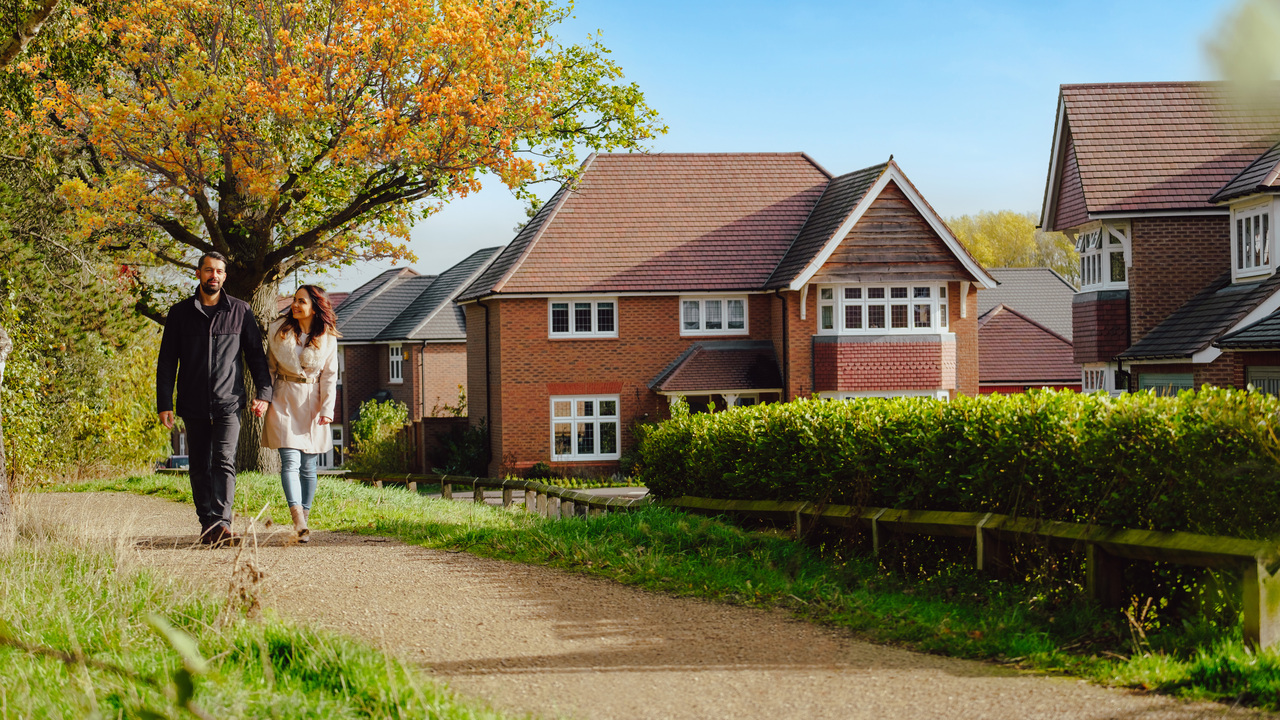 Couple walking down a tree-lined path next to a Redrow development
