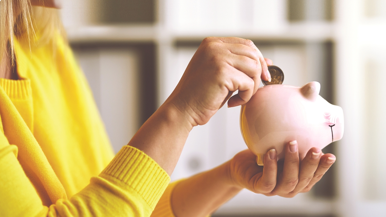 Woman in a yellow jumper placing a coin in a piggy bank