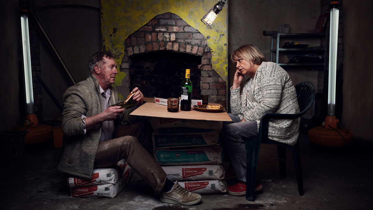 Fed-up looking, dust-covered couple eating dinner in the rubble of their home renovation