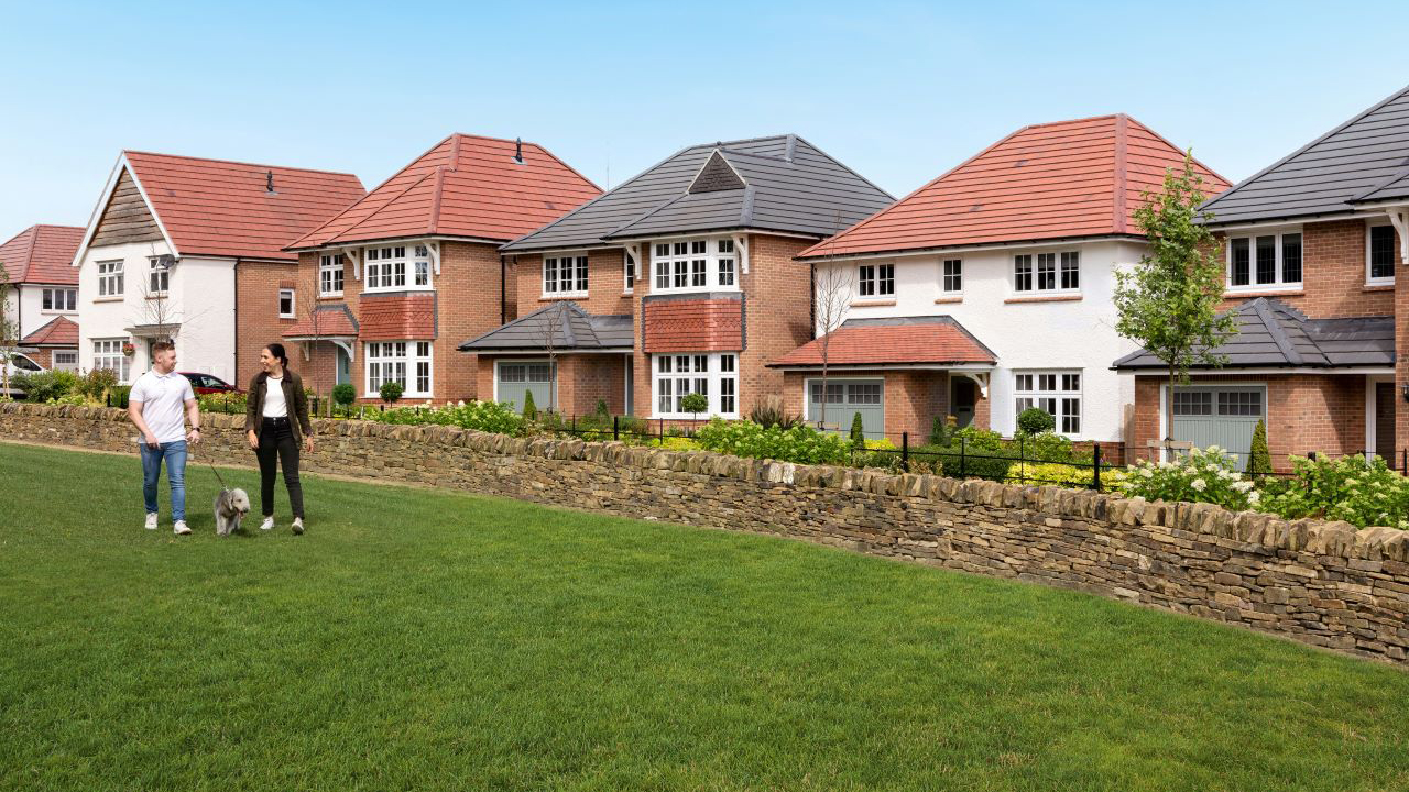 Two people walking a dog on some grass opposite a row of Redrow homes
