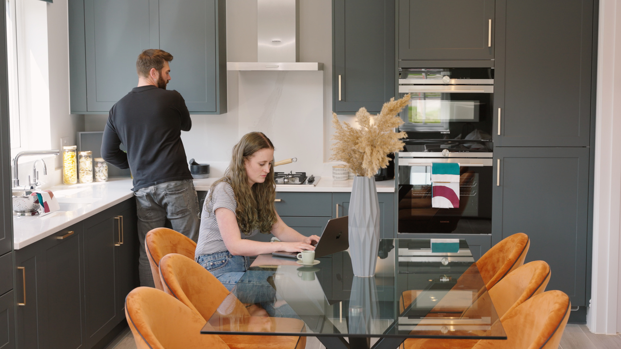 Woman on laptop and man making coffee in a kitchen together