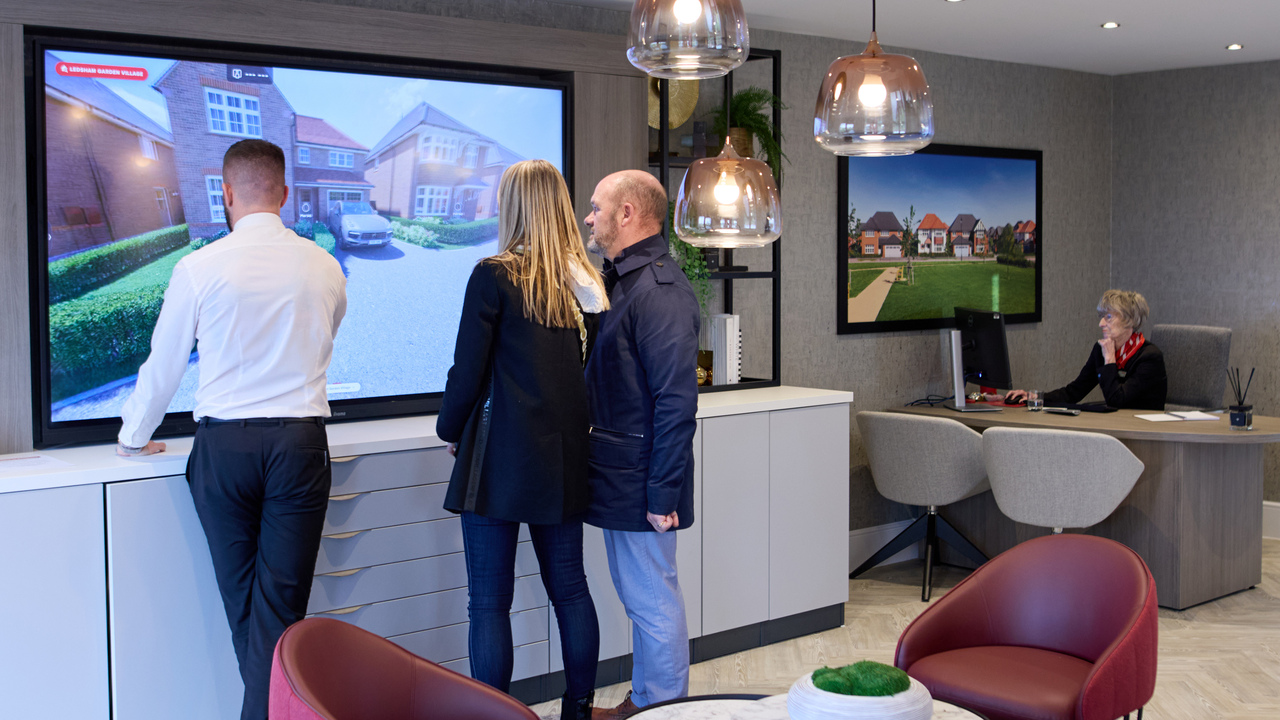 A Redrow sales consultant showing a couple a house on a large screen in the customer experience suite