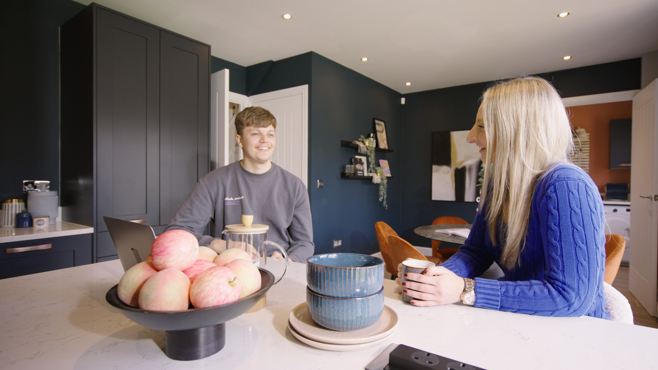 Couple sat at a breakfast bar looking at a laptop and laughing