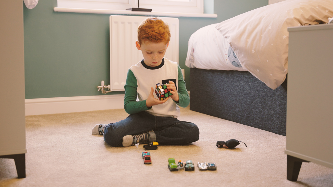 A boy with ginger hair playing with toys on the floor of a green bedroom