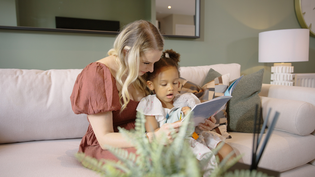 Mum and child reading a book together on a beige sofa in a green lounge
