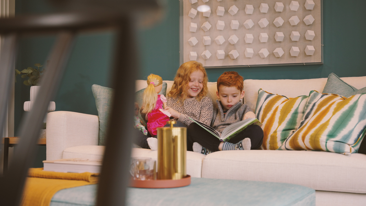 Two small children sat on a couch reading a book together