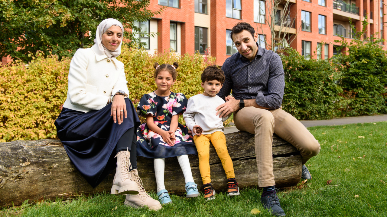 Couple and their two children sitting on a log outside an apartment block