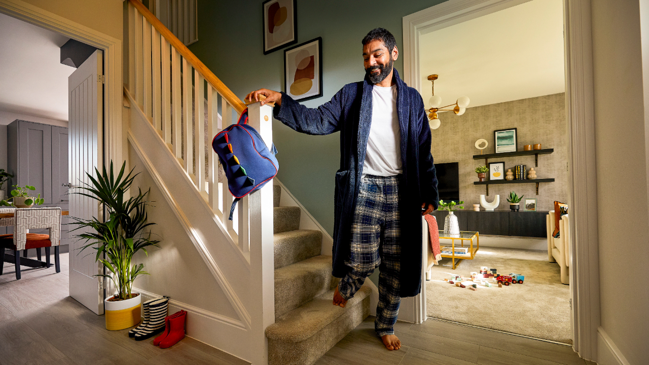 Man in a dressing gown walking barefoot down carpeted stairs onto underfloor heated floorboards