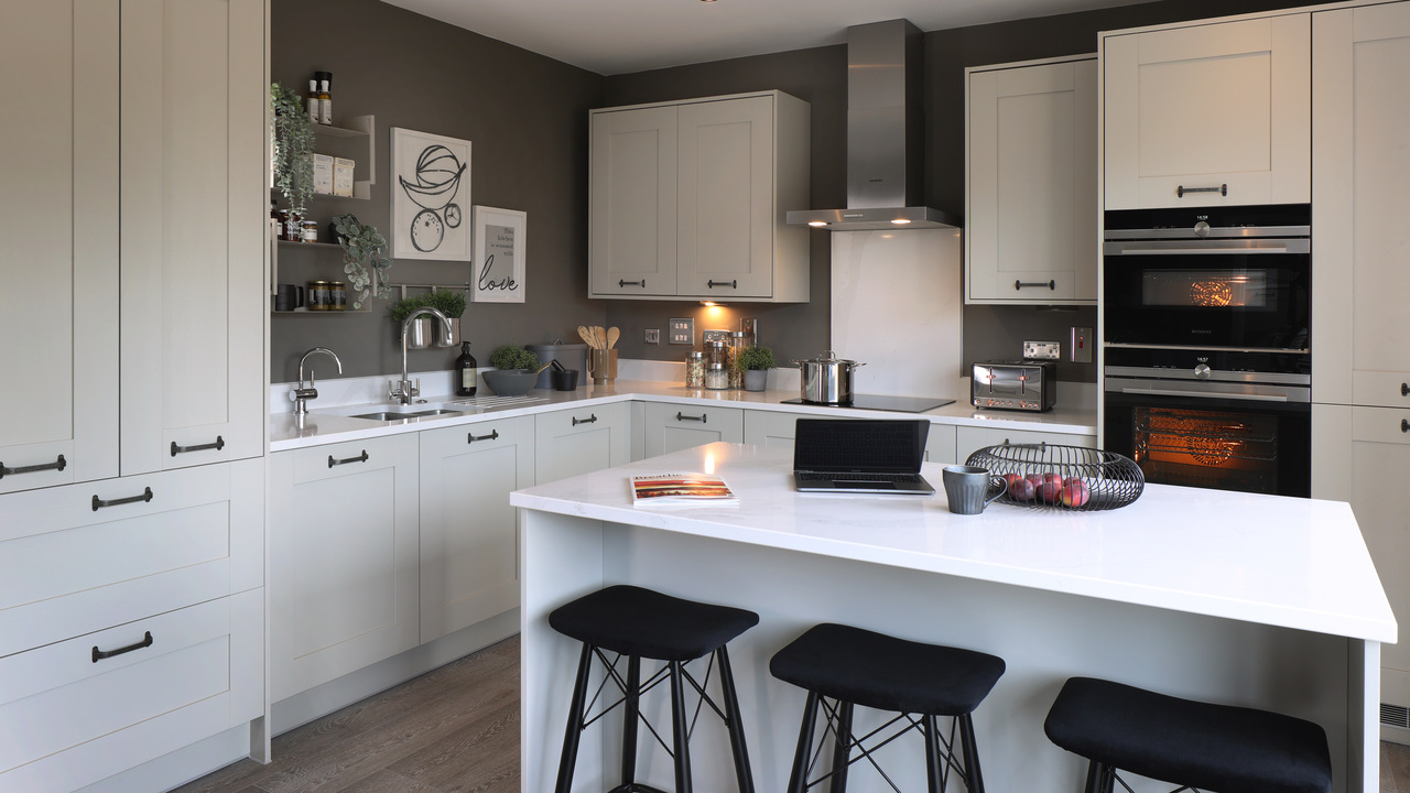 Large, white kitchen with three barstools beside a kitchen island
