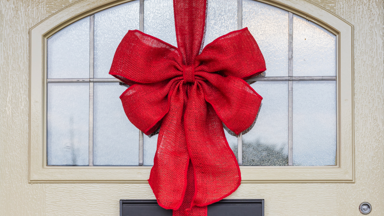 Red bow gift wrapping a grey front door with an arched window