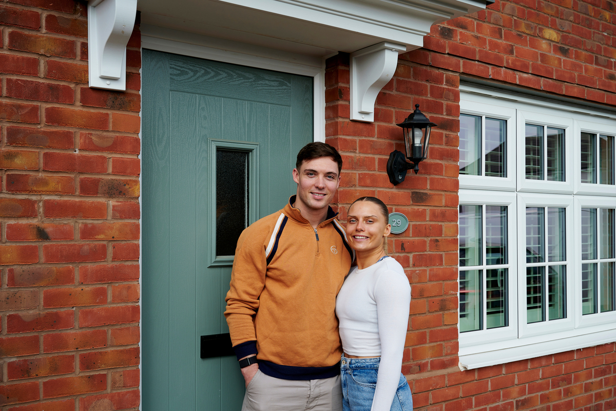 A young couple in front of their new build home from Redrow home  