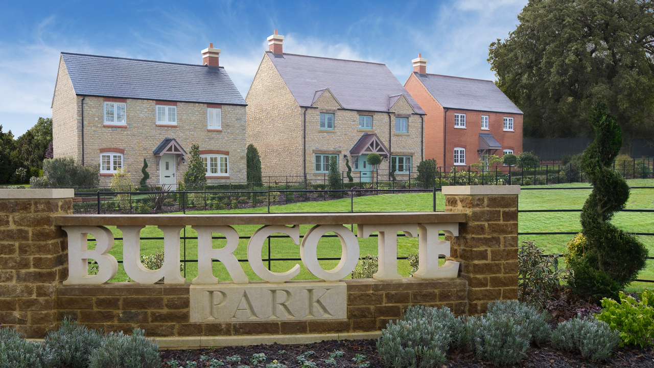 A row of houses behind a large sign saying Burcote Park
