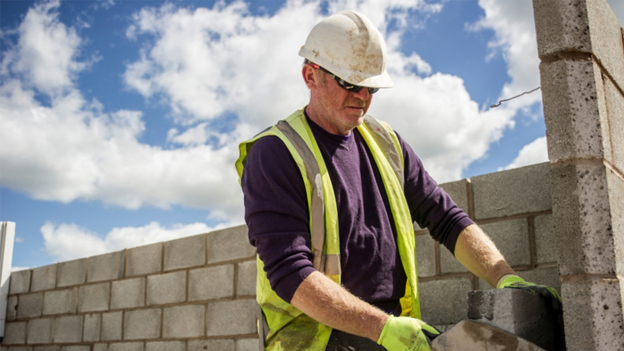 Construction worker in a hard hat and hi-vis building a wall