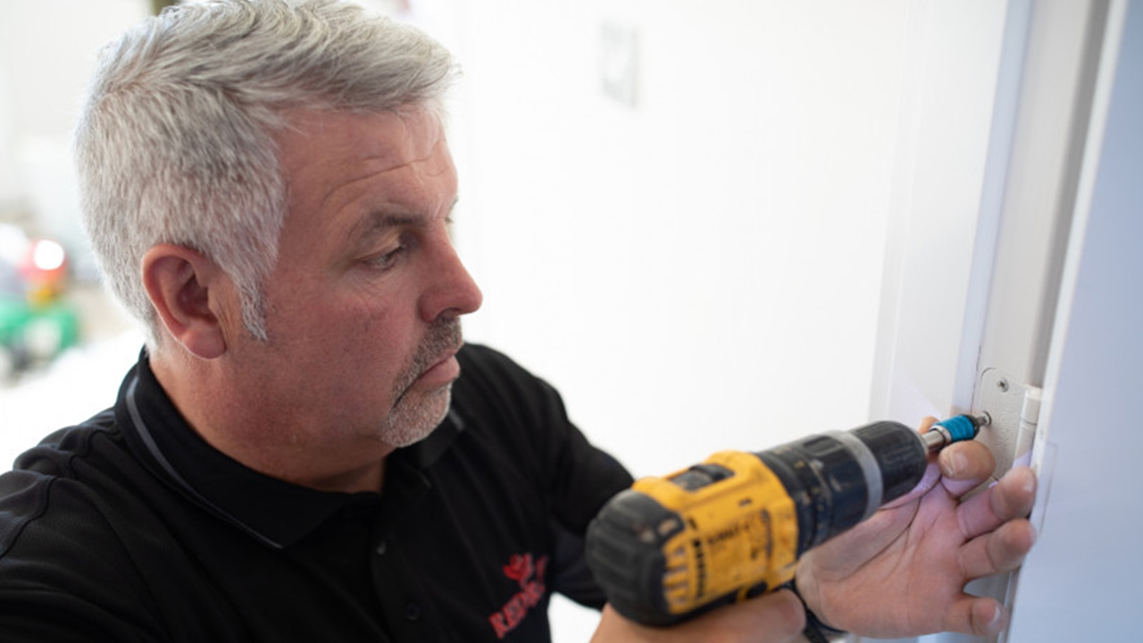 Man using a yellow drill to add screws to a door frame