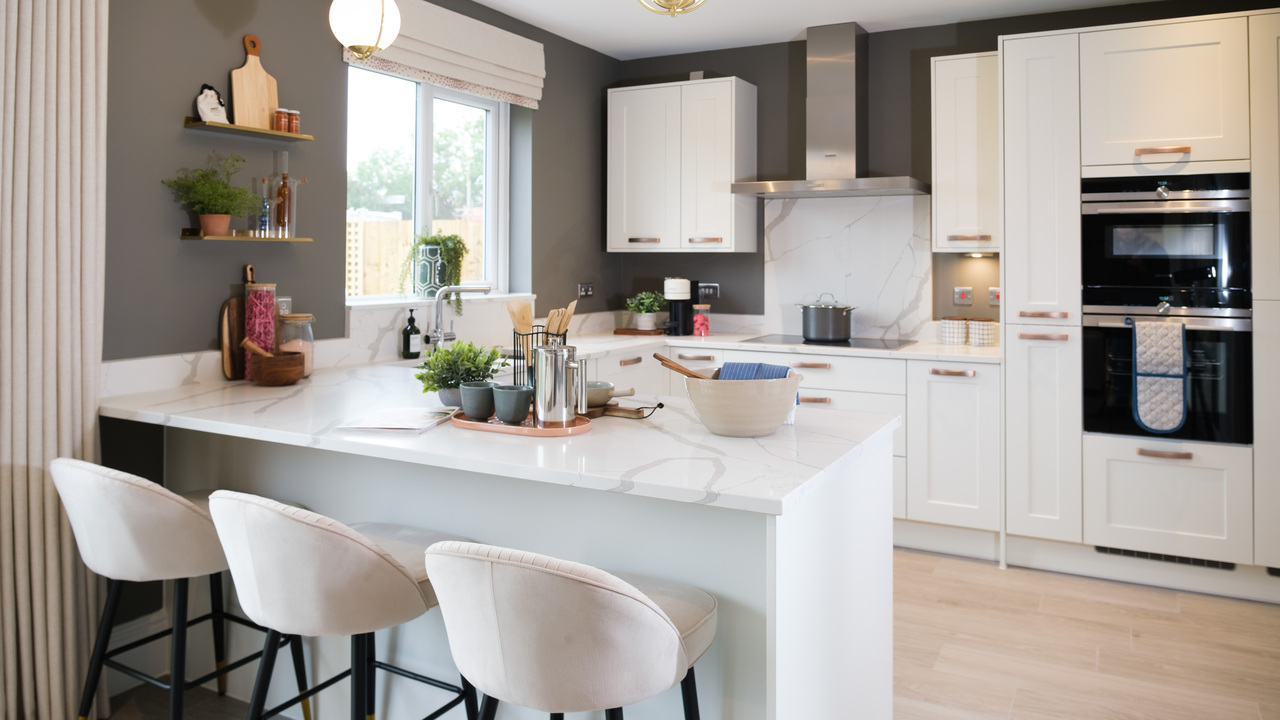 White kitchen with three barstools in front of a marble-topped breakfast bar