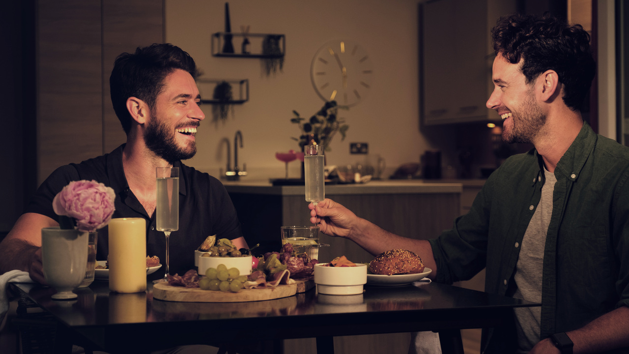 Two men laughing and sharing a deli board as they make a toast in their new home