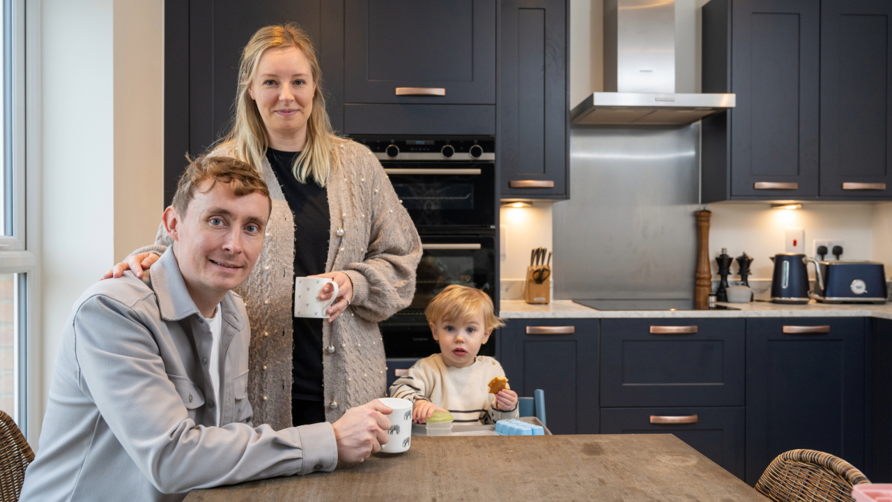 Couple drinking hot drinks in a navy kitchen and a baby eating a snack in a high chair
