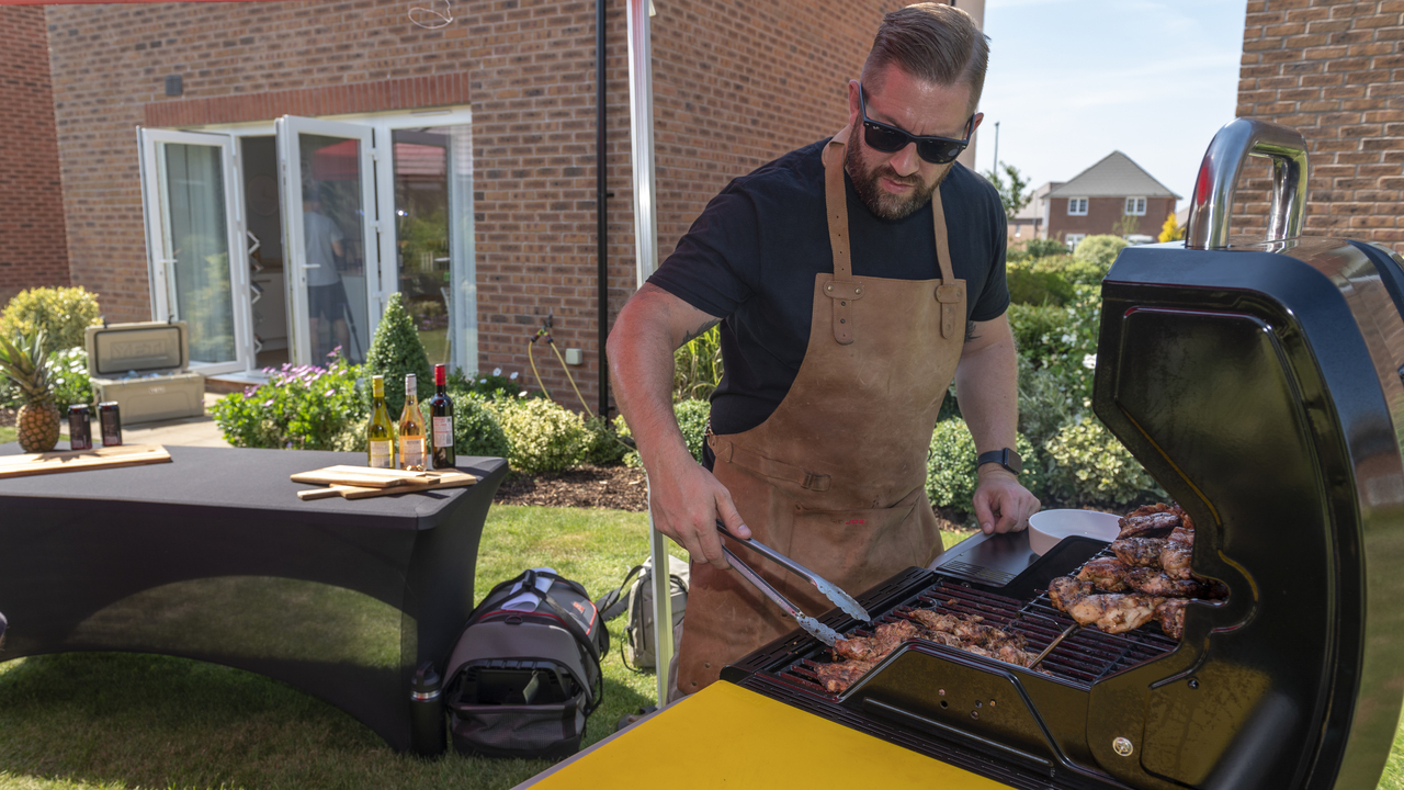 Man at a BBQ turning chicken wings with some tongs