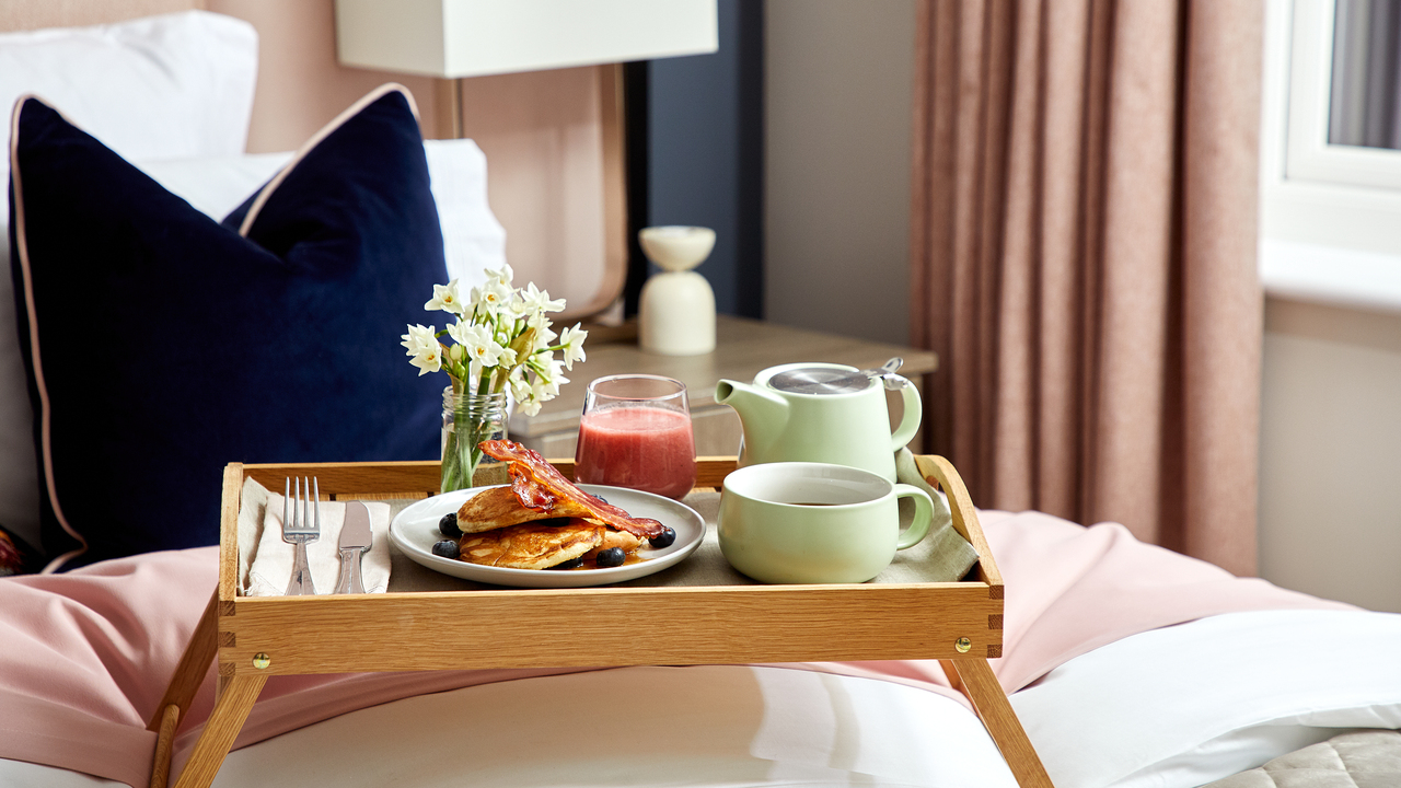 Breakfast tray on a bed with pancakes, tea and juice