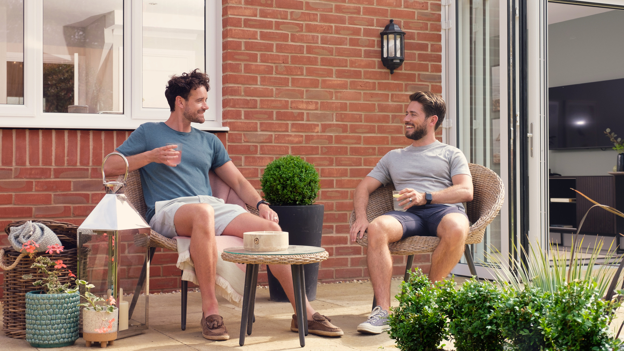 Two men sitting on wicker chairs enjoying a drink in their garden
