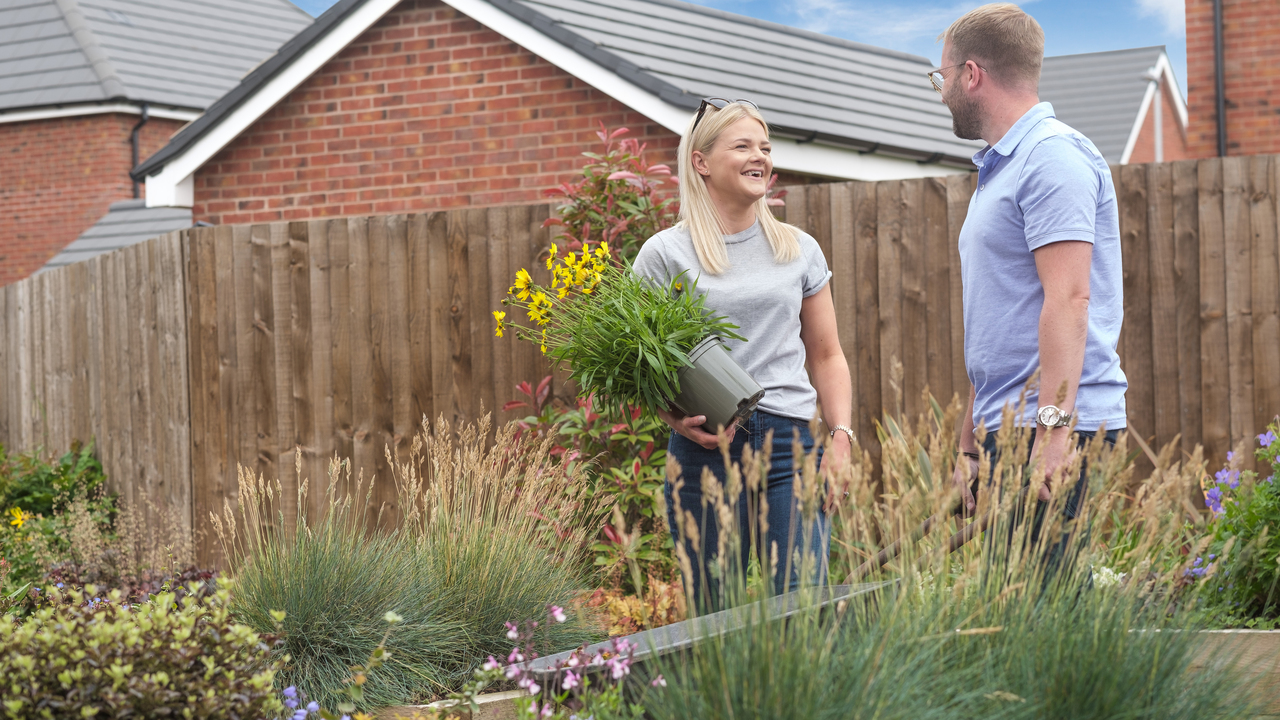 Woman holding a pot of yellow flowers laughing and talking to a man in a garden