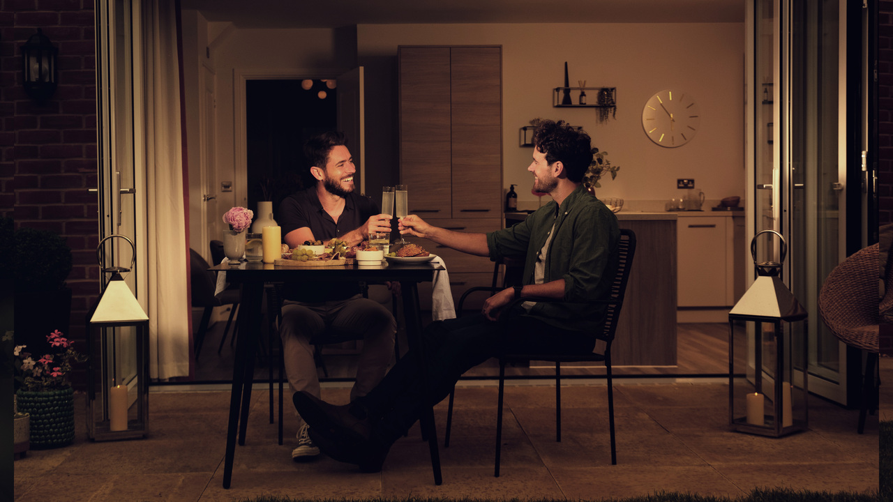 Two men raising a toast as they dine alfresco in their garden at night