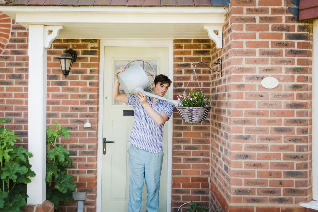 Man watering flowers in a hanging basket outside his house