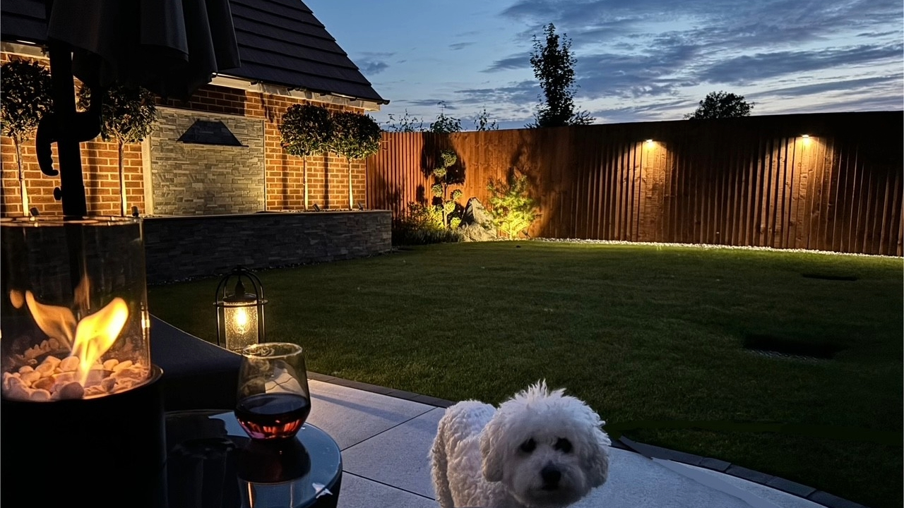 Garden at night with relaxing downlights, firepit and a small white dog