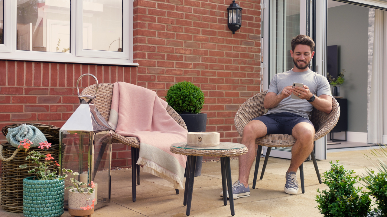 Man sitting on wicker garden furniture smiling as he checks his phone